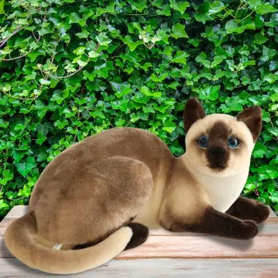 Peluche chat réaliste assis entre les feuilles vertes peluche chat